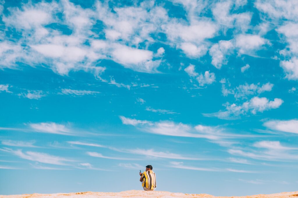 man and woman walking on brown sand under blue sky and white clouds during daytime